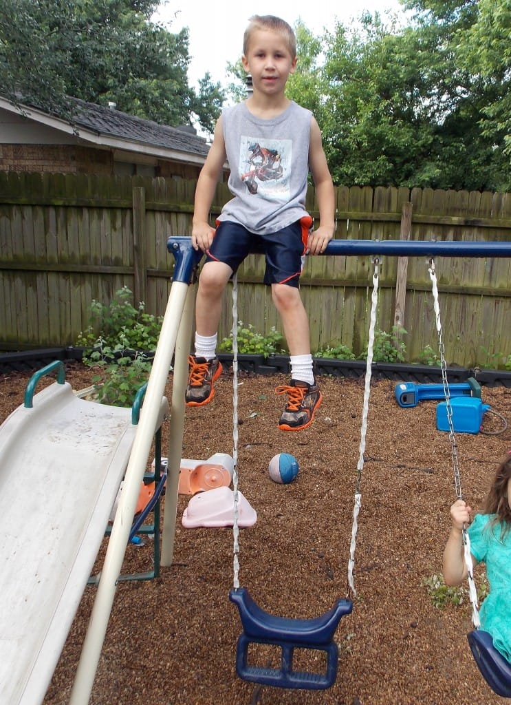 school age child sitting on top of the swing set bar