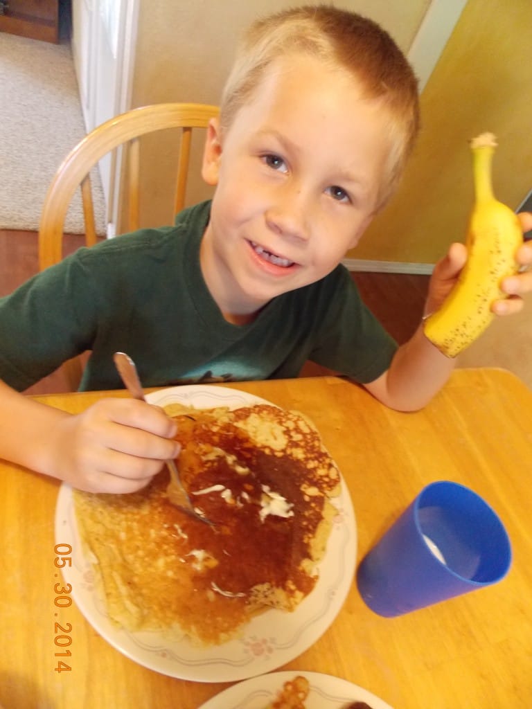 child eating whole grain pancake and banana with cup of milk