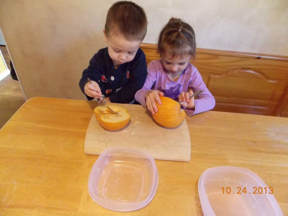 Kids exploring pumpkins by scraping out pumpkin guts and seeds with a spoons