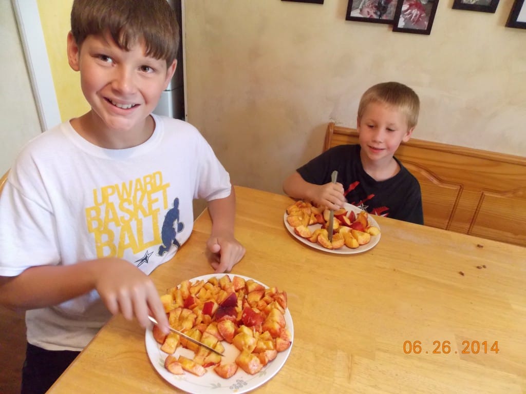 kids at the table cutting up fresh peaches with butter knives for peach yogurt pops