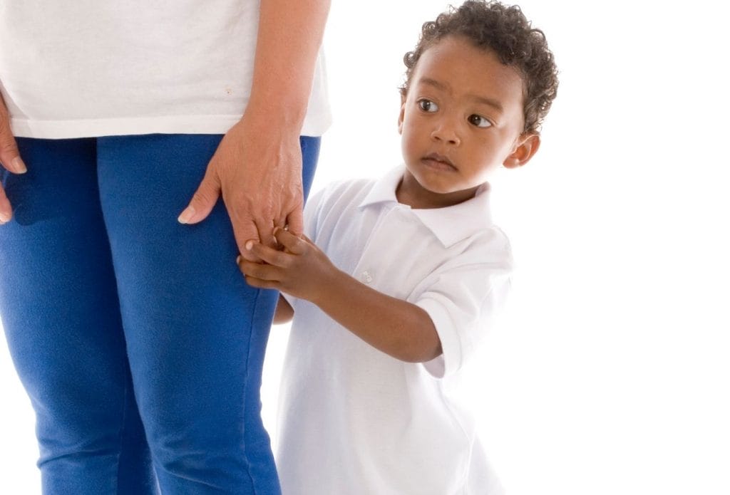 child with separation anxiety looking scared behind mom