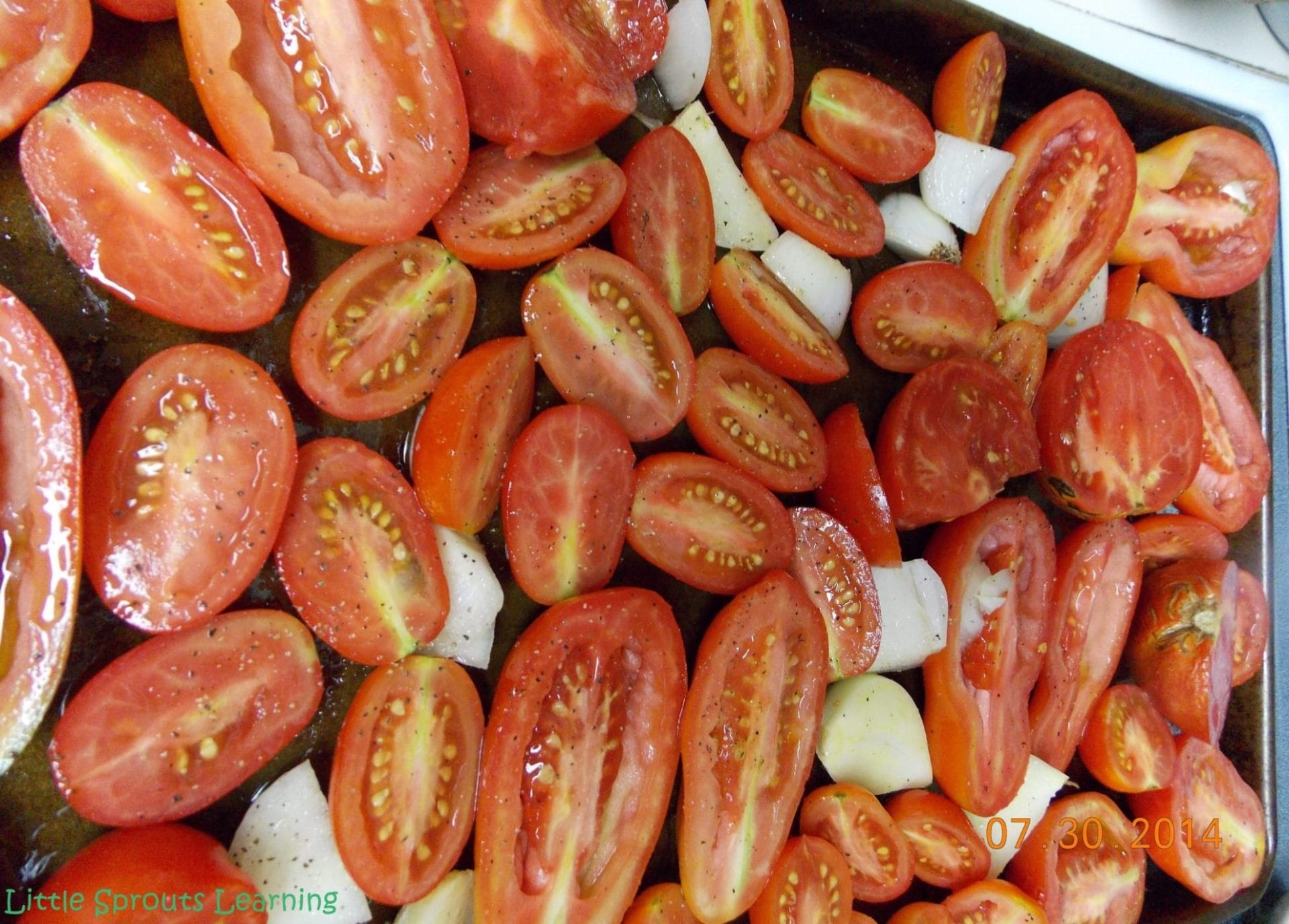 tomatoes, onions and garlic tossed in olive oil, salt and pepper on a sheet pan ready to go in the oven to roast.