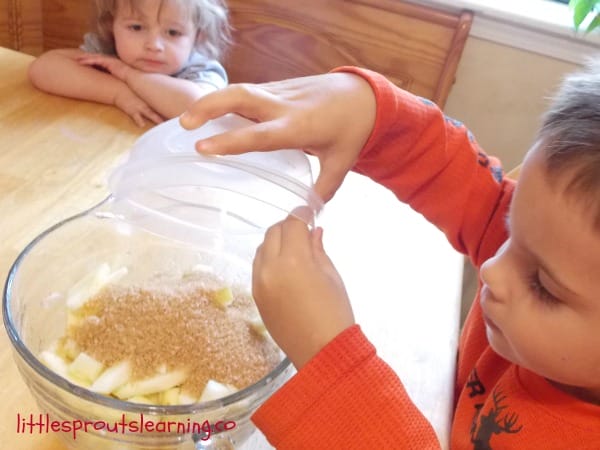 Old fashioned apple crisp recipe being made by young children, child pouring sugar into apples
