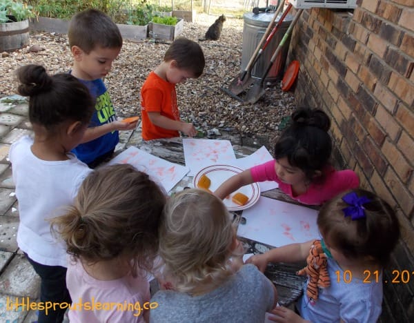 kids doing pumpkin stamping with ink pads and paper on a table outside