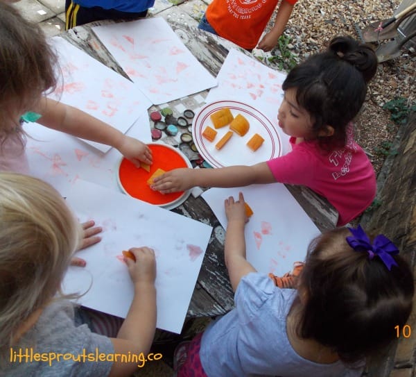 kids around a table with stamp pads and pumpkin stamps stamping them on paper.