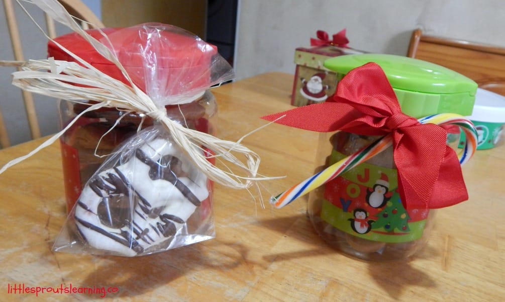 Cute gift packaging for homemade gifts, two plastic jars full of christmas candies and tied with a bow, one with a candy cane in it and one with a chocolate covered pretzel. 