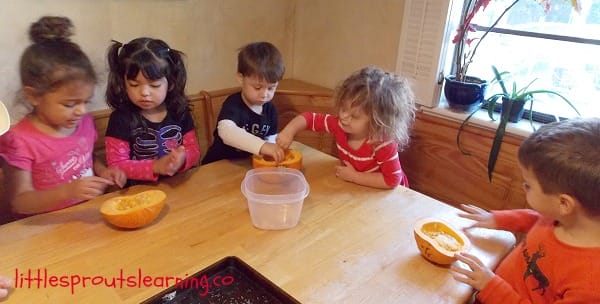 young children at the table scooping seeds and goop out of pumpkins
