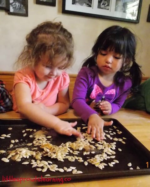Two girls spreading pumpkin seeds out on a baking pan