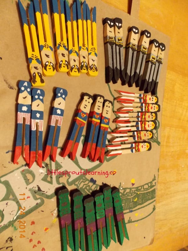 Finsihed superhero ornaments drying on a paper sack. Clothespin superhero ornaments. Wolverine ornaments, bat man ornaments, captain america ornaments, superman ornaments, hulk ornaments, and wonder woman ornaments.