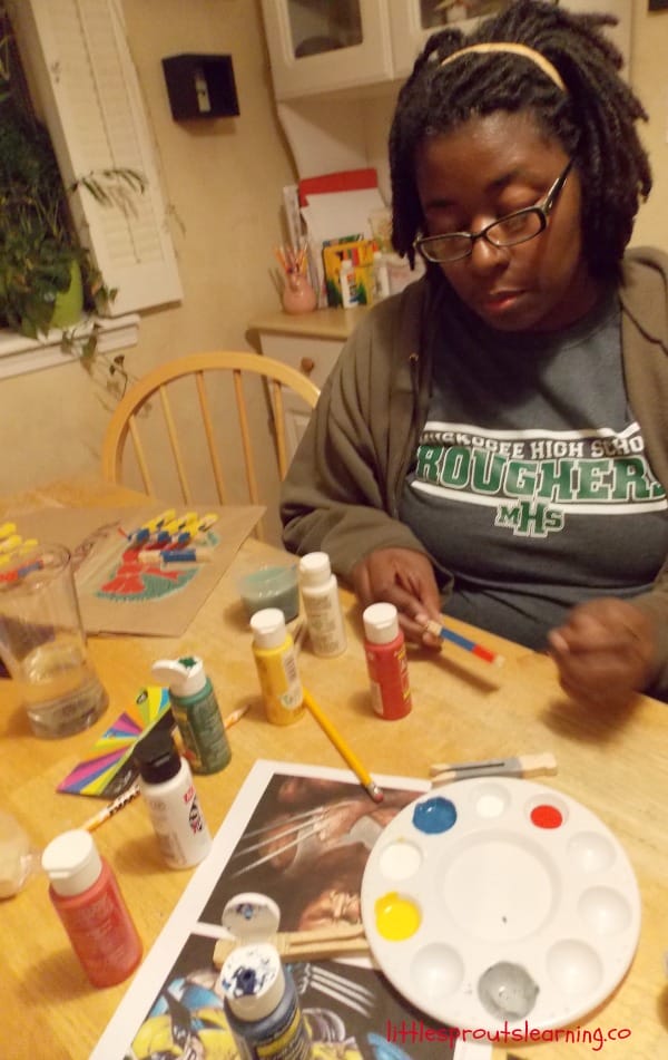 superhero ornaments being painted by a woman at the table.