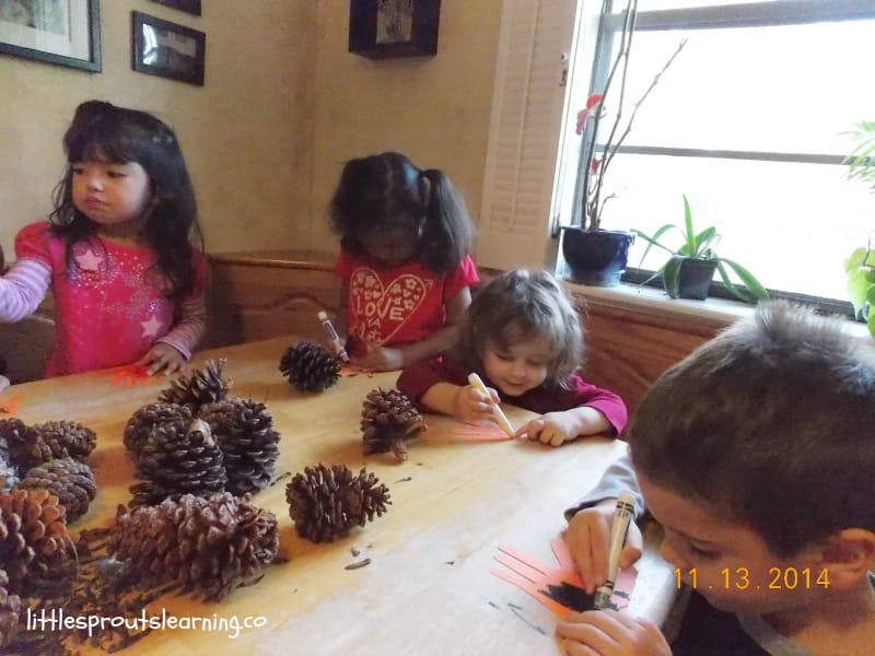 daycare kids doing activities at the table with hand prints, markers and pinecones
