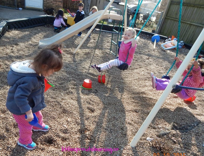 Kids playing outside, some swinging, some digging in pea gravel, some playing with a shopping cart, the importance of play in early childhood settings.