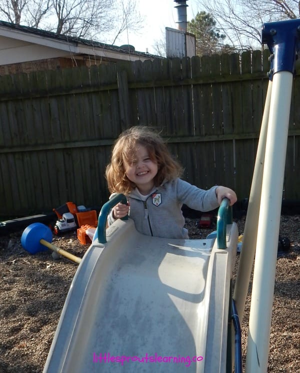 child enjoying play in early childhood setting by climbing up a slide outside. Shes smiling and having fun.