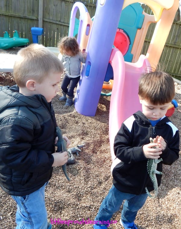 kids playing with dinosars and crocoldiles outside on the playground.
