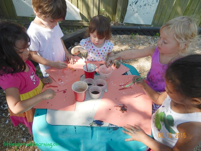kids at a table with paints painting on paper
