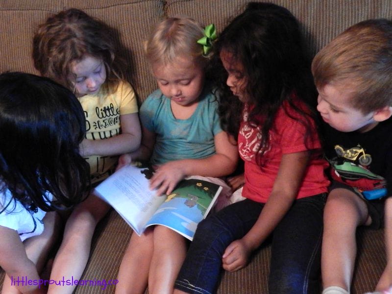 5 kids sitting on the couch looking at a book together reading