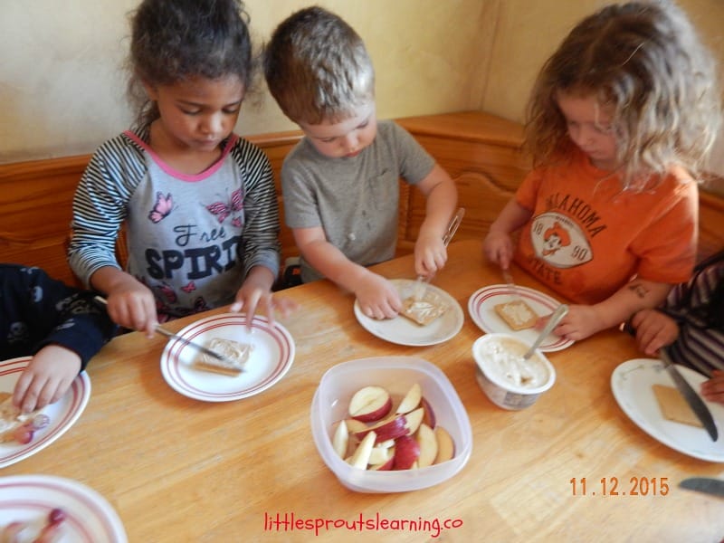 kids at the table spreading cream cheese sauce on graham crackers to make fruit pizza recipe for kids