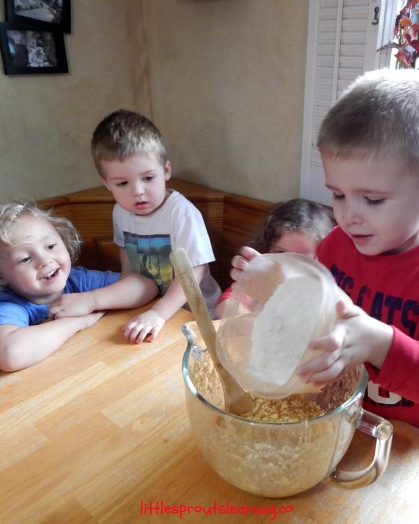 kids cooking, one child dumping flour into a mixing bowl while other kids watch.
