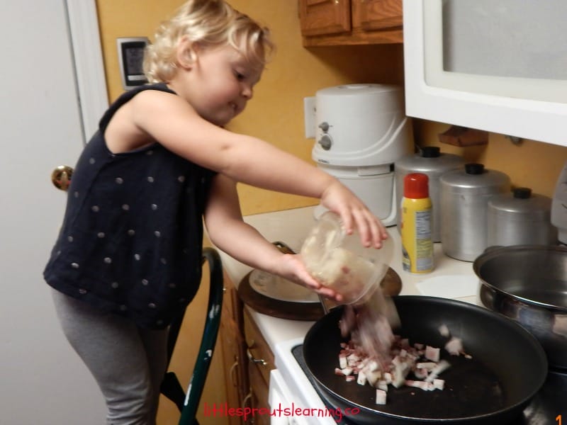 Lotsa Pasta Recipe-Kids cooking classes. Child standing at the stove putting bacon in a skillet to brown.