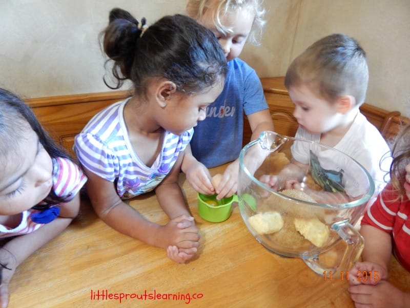 Making cookies with kids, children cracking eggs and putting ingredients in a bowl at the table.