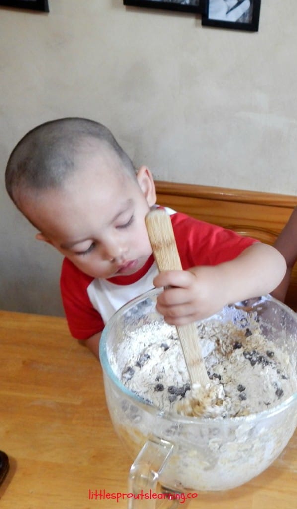  small child holding a spoon stirring thick cookie dough
