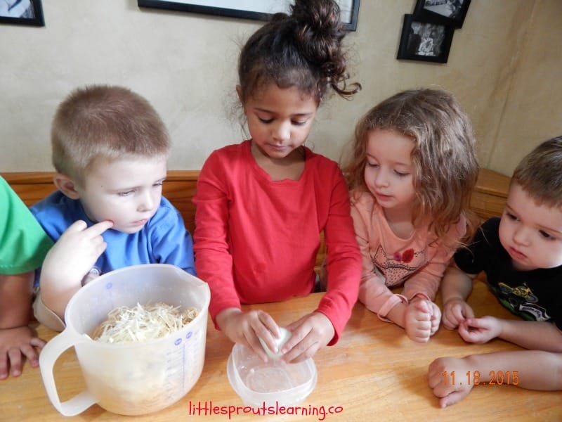 kids cooking spaghetti pie, cracking an egg at the table while other kids watch