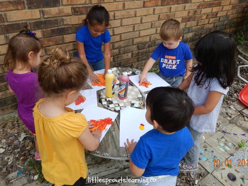family childcare kids finger painting on paper on a table outside.