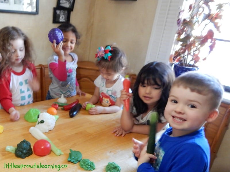 kids at the table with plastic fruits and vegetables playing a healthy food game.