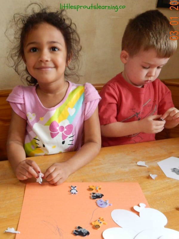 two kids at the table with different types of paper and different types of art medium, stickers, crayons, to make whatever they create.