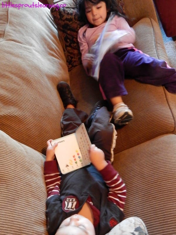 two kids laying on the couch with books.