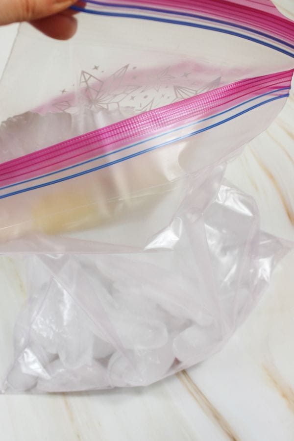 A hand holds open a clear ziplock bag containing several ice cubes, perfect for making an ice cream in a bag recipe.