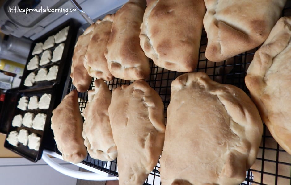 ham and cheese homemade hot pockets on a cooling rack fresh from the oven next to raw hot pockets ready to go in the oven.