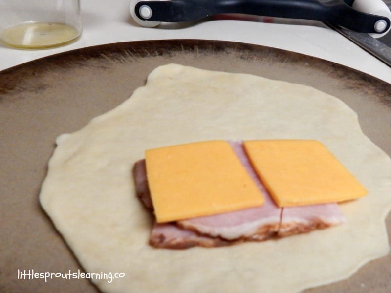 dough rolled out and topped with slices of ham and cheese on a rolling board.