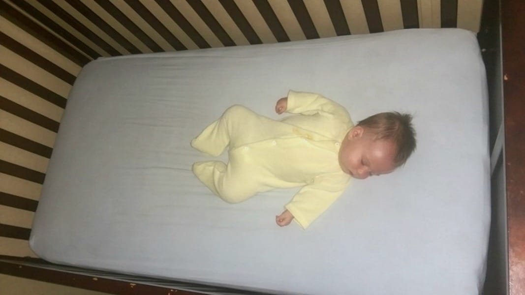 baby safely sleeping on their back in a crib with a tight fighting sheet and no blankets or toys