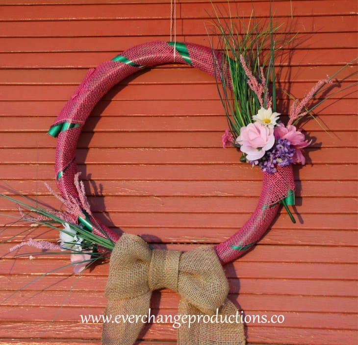 hose wreath made of upcycled hose, burlap ribbon, and decorated with flowers hanging on a door