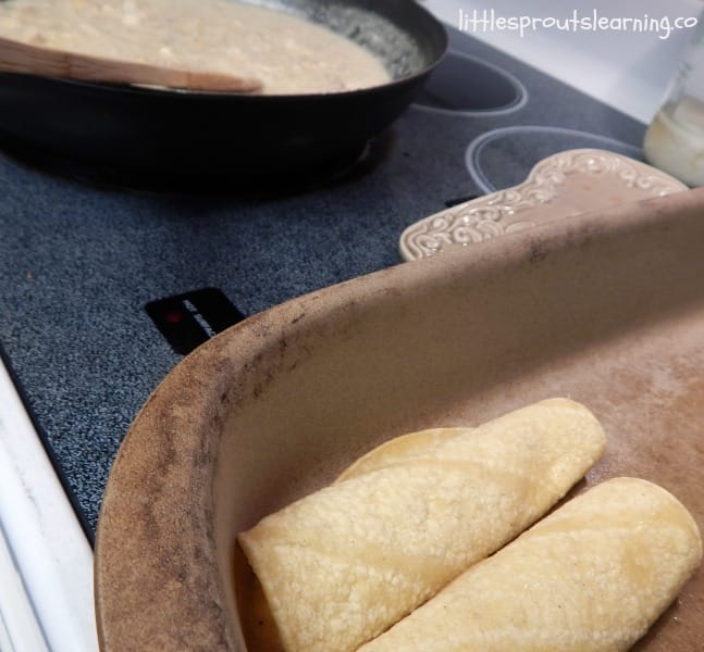 skillet full of enchilada stuffing and a pan with two rolled enchiladas