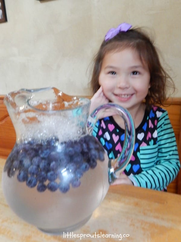 Girl smiling with a pitcher of blueberry soda.