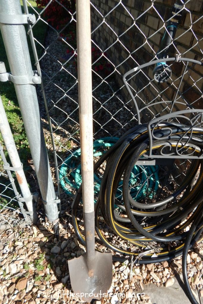 a garden shovel by a fence and a hose
