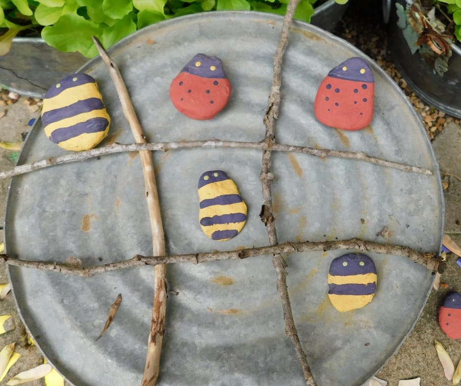 garden tic tac toe game made out of painted rocks and sticks on a bucket.