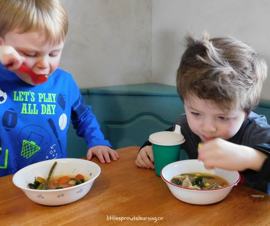 two boys sitting at a table eating stone soup or friendship soup