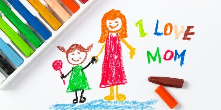 Crayon drawing of mom and daughter that says I love mom with crayons on the table