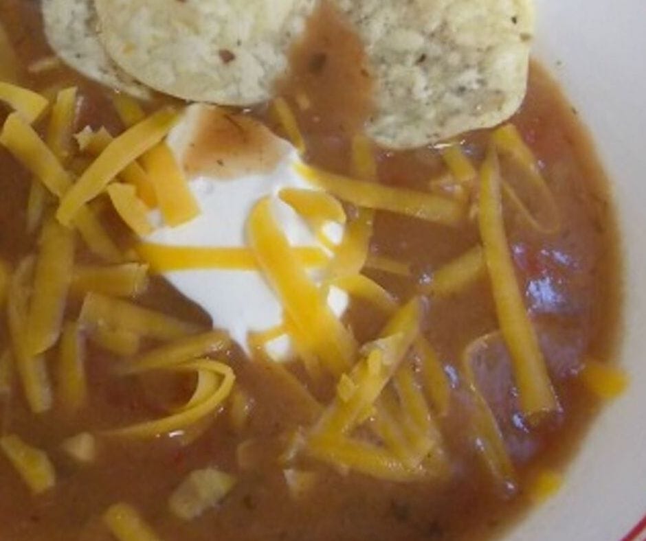 crock pot taco soup in a bowl topped with a dollop of sour cream some shreds of cheese and a few tortilla chips