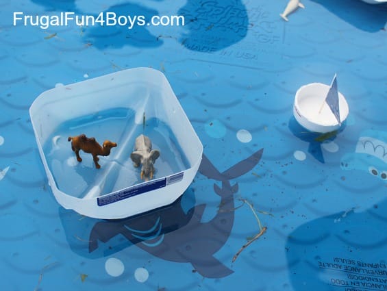 recycled boats floating in a small swimming pool. One is made of the bottom of a milk carton and has animals riding in it, the other is the bottom of a styrofoam cup with a small sail.