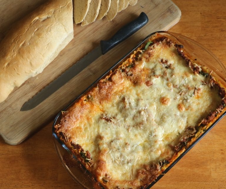 vegetable meat lasagna in a dish by a cutting board with bread