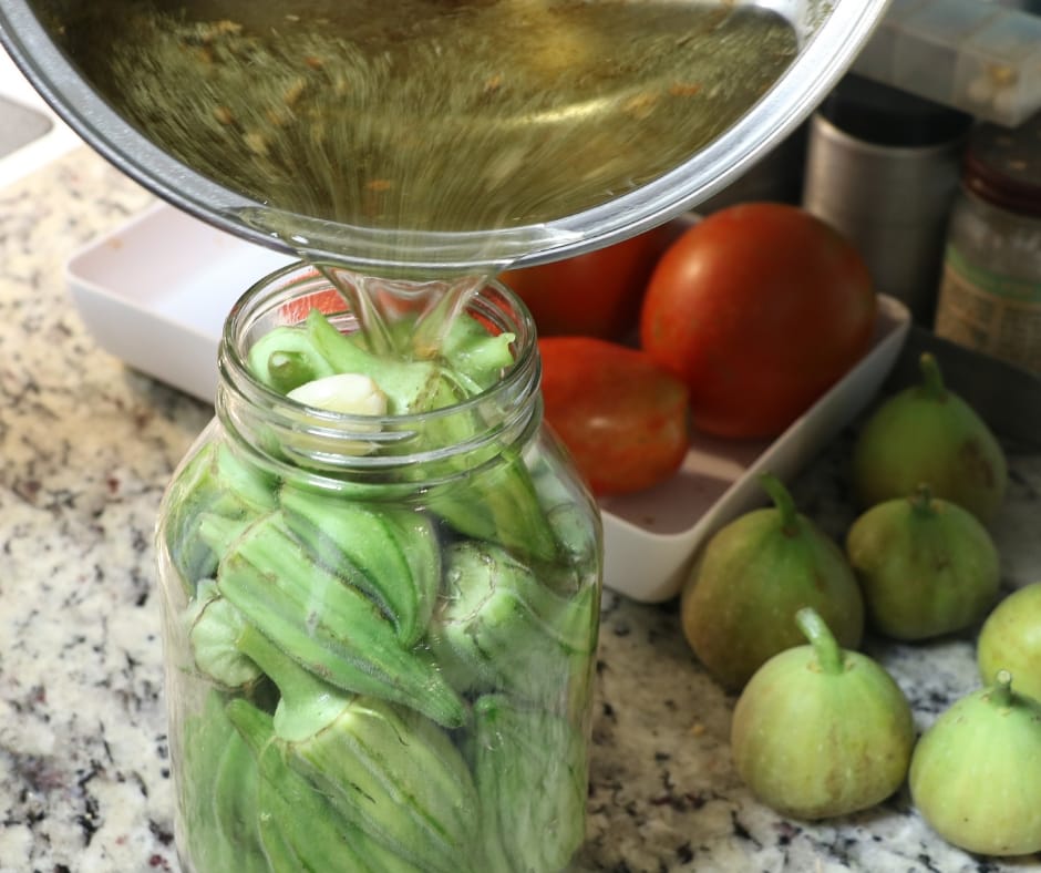 pouring brine onto jar of okra for pickling