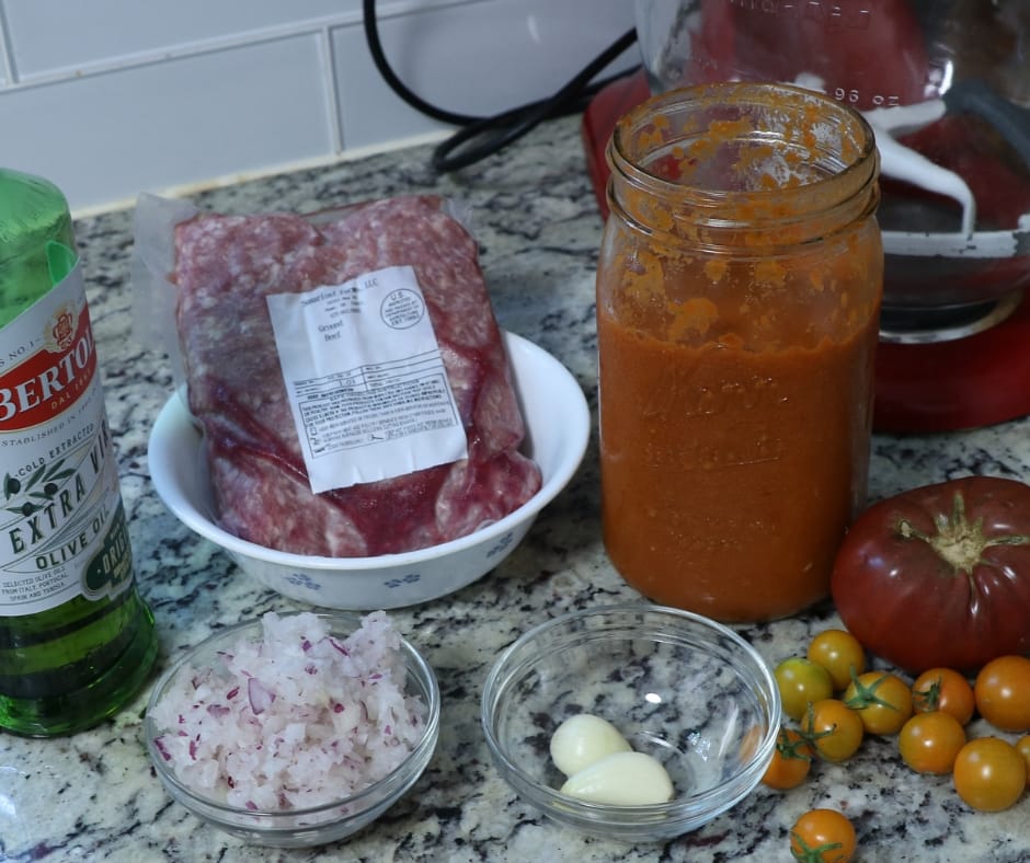 Spaghetti sauce ingredients on the counter, oven roasted tomato sauce, garlic, onions, olive oil, ground beef