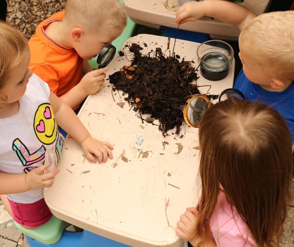 Kids looking at the contents of compost and soil with magnifying glasses