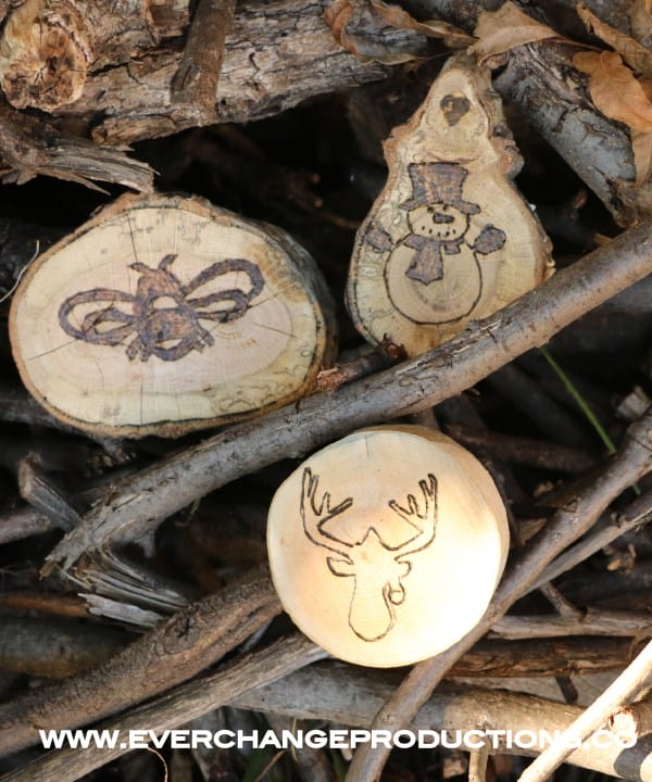 Three wood burned wood slice ornaments arranged in a wood pile