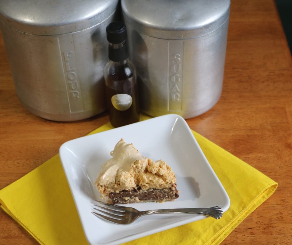 slice of grandma's chocolate pie on a plate with a fork on a napkin in front of flour canister, sugar canister and bottle of chocolate extract