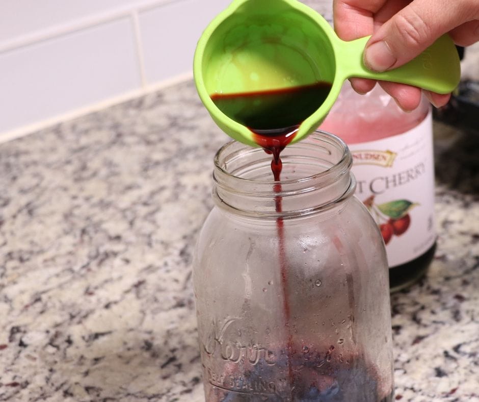 Pouring cherry juice into mason jar to make cherry limeade